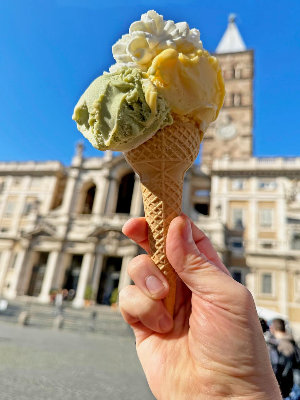 A pistachio and lemon gelato in a cone held in front of Santa Maria Maggiore basilica in Rome