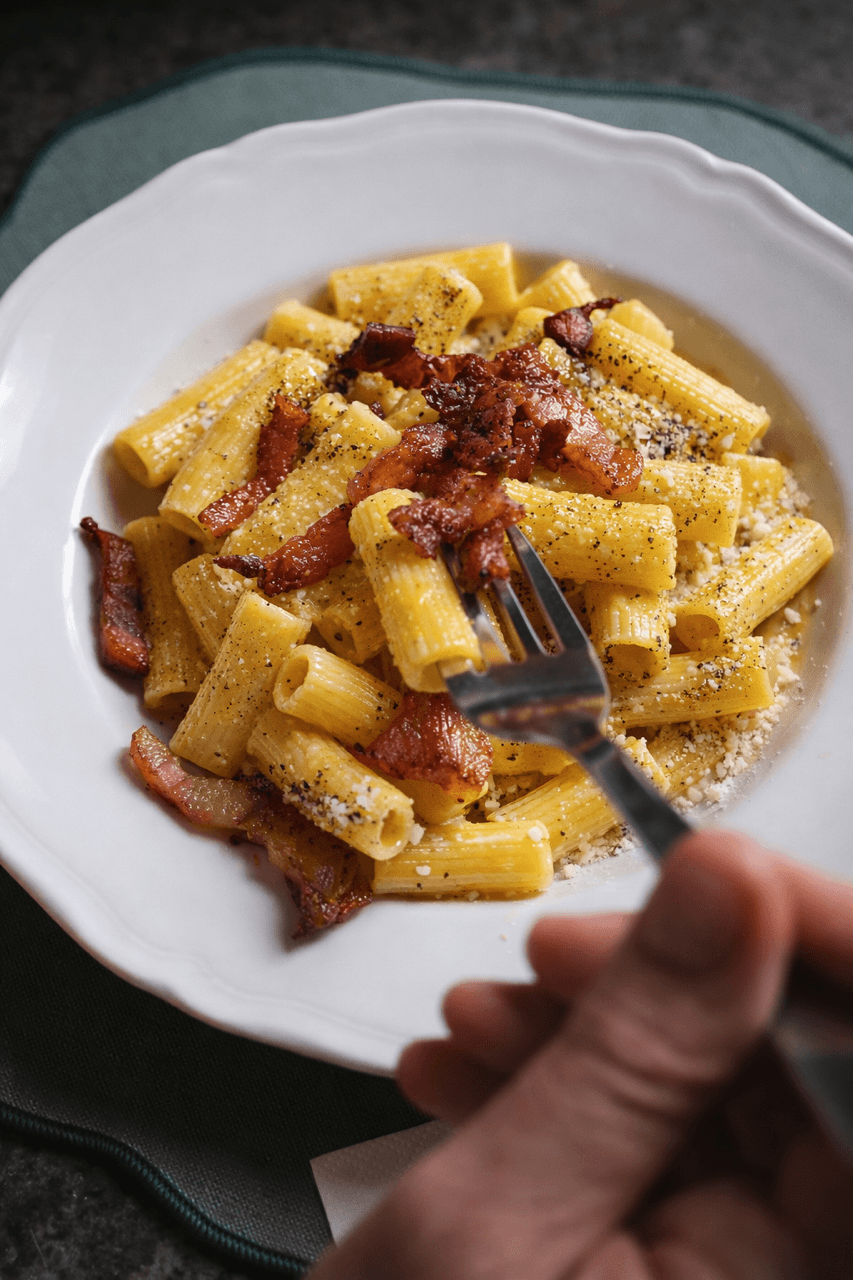 A plate of rigatoni alla carbonara with crispy guanciale and Pecorino, photographed in a Roman trattoria